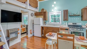 A kitchen with wooden cabinets, a refrigerator, a stove, and a dining area with a table and chairs. - Secluded Vacation Rental Bordering Creek! (Mountain View)