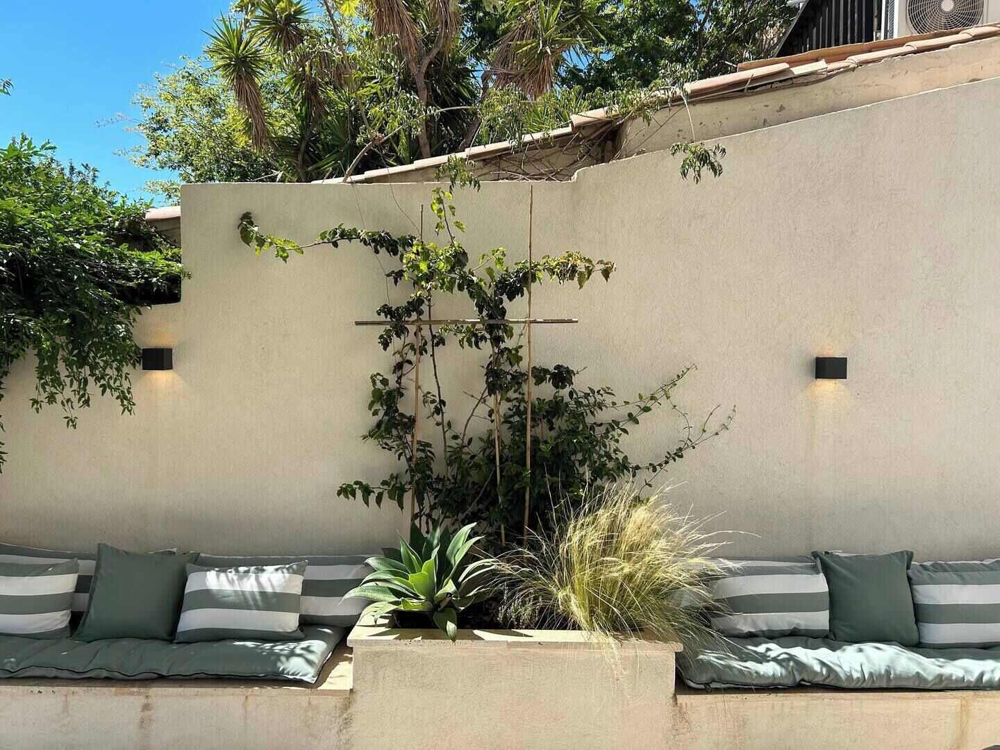 A modern outdoor seating area with a concrete wall, a climbing plant, and a small planter with a plant.