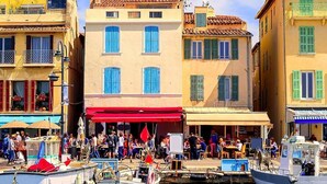 A bustling waterfront with colorful buildings, a dock with boats, and people dining outside. - A DAY AT LA VILLA BOMPARD: RELAXATION AND ADVENTURE AWAIT (Marseille)