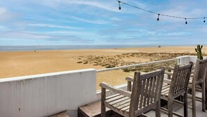 Uitzicht op het strand vanaf een balkon, met houten stoelen en een lichtslingering.
