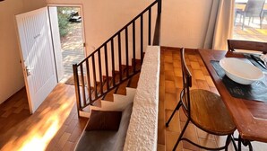 Een trap die leidt naar een balkon met een houten tafel en stoelen, een deur en een lijst met een afbeelding aan de muur.