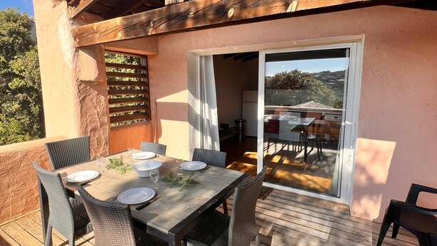 Een eethoek buiten met een houten terras, een tafel gedekt voor vier personen, en uitzicht op het omliggende landschap door een glazen deur.