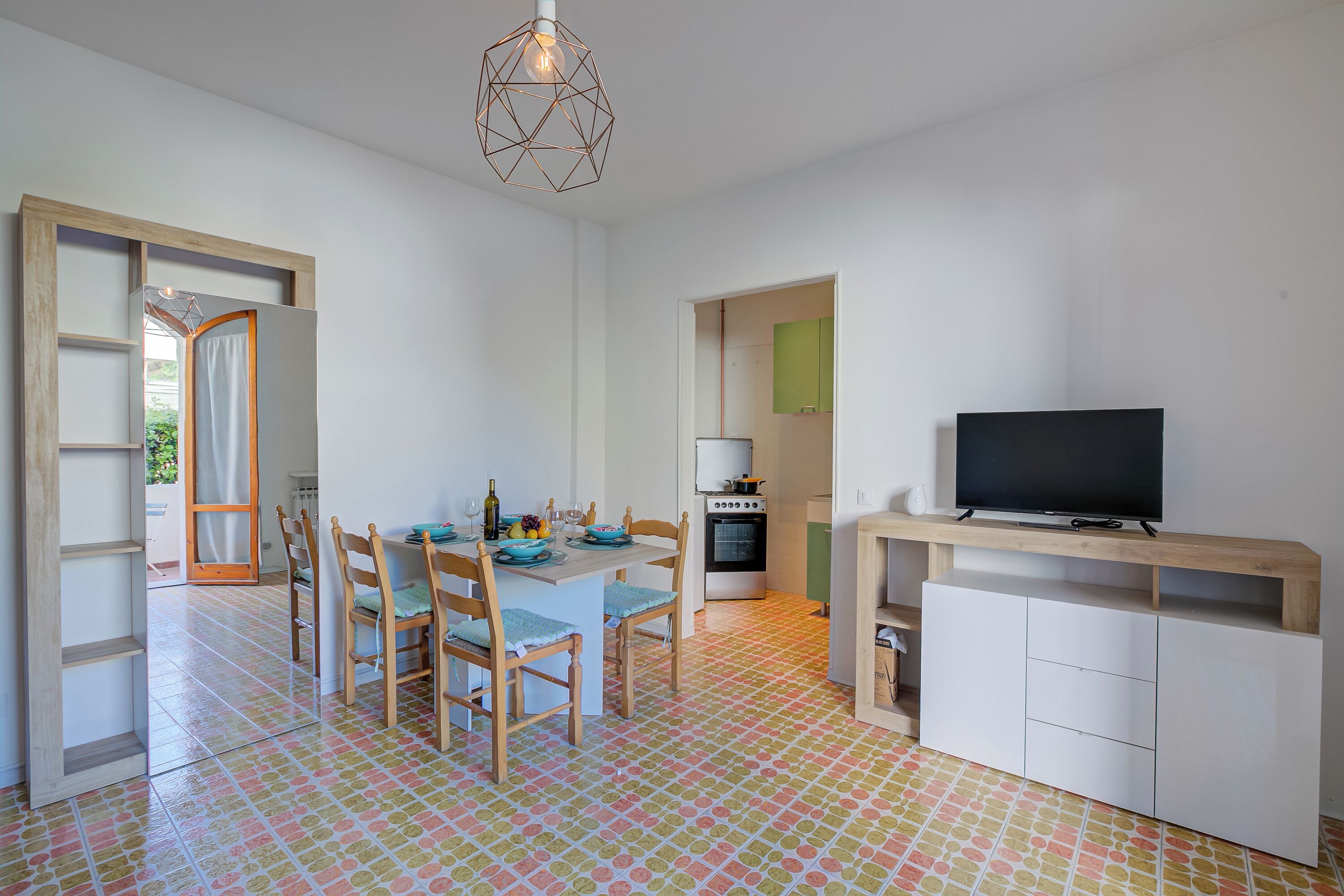 Une cuisine compacte avec un coin repas, un téléviseur posé sur un meuble en bois et un sol carrelé.