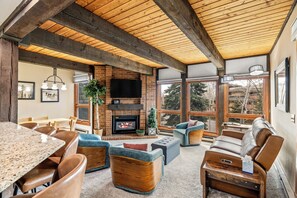 A spacious living area with a fireplace, comfortable seating, and large windows offering a view of the outdoors. - Corner Condo Near Gondola | 2BR Retreat w/ Pool, Hot Tubs and Deck Views! (Steamboat Springs)