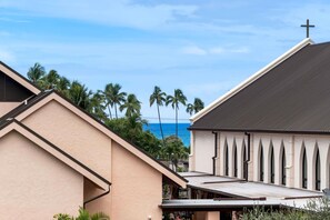 A church with a cross on the roof, surrounded by palm trees and a view of the ocean. - Kailua Village #201: 2nd Floor, Corner Remodeled unit in Downtown Kona. (Kailua-Kona)