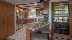 Une cuisine dotée de plans de travail en granit, de meubles en bois, d’un r éfrigérateur en acier inoxydable et d’un îlot central intégré avec des tabourets de bar.