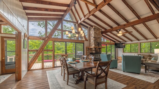 Une pièce spacieuse avec un plafond en bois, de grandes fenêtres, une table à manger avec des chaises et un coin salon confortable.