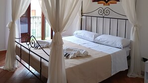 A four-poster canopy bed with white bedding and curtains, a decorative headboard, and a view of the outdoors through a window. - A casa di Peppe (Palermo)
