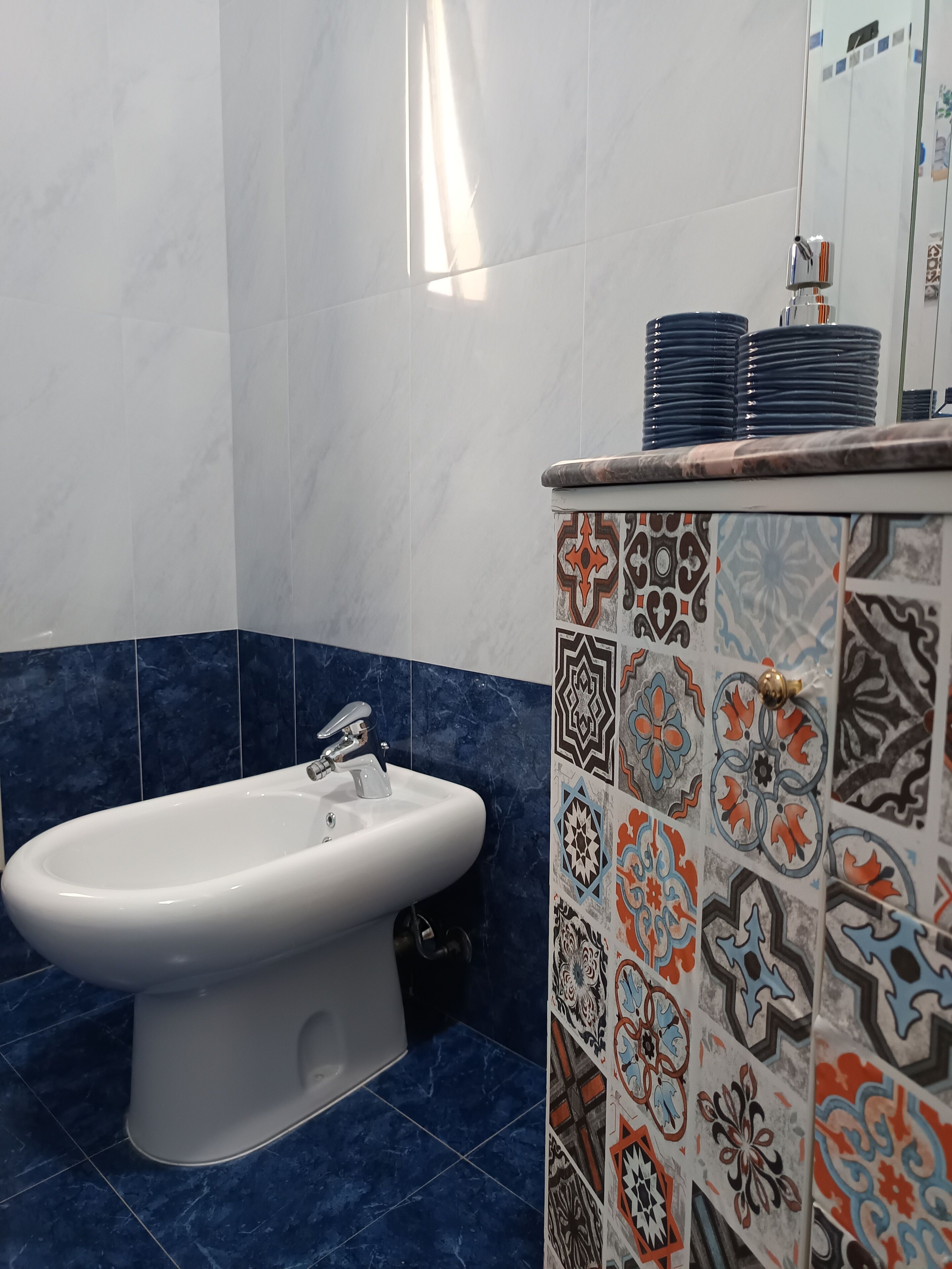 A bathroom with a bidet, a sink, and a tiled wall with a decorative pattern.