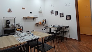 A dining area with a wooden table set for four, black chairs, a coffee machine, and a shelf with kitchen items. - A casa di Peppe (Palermo)