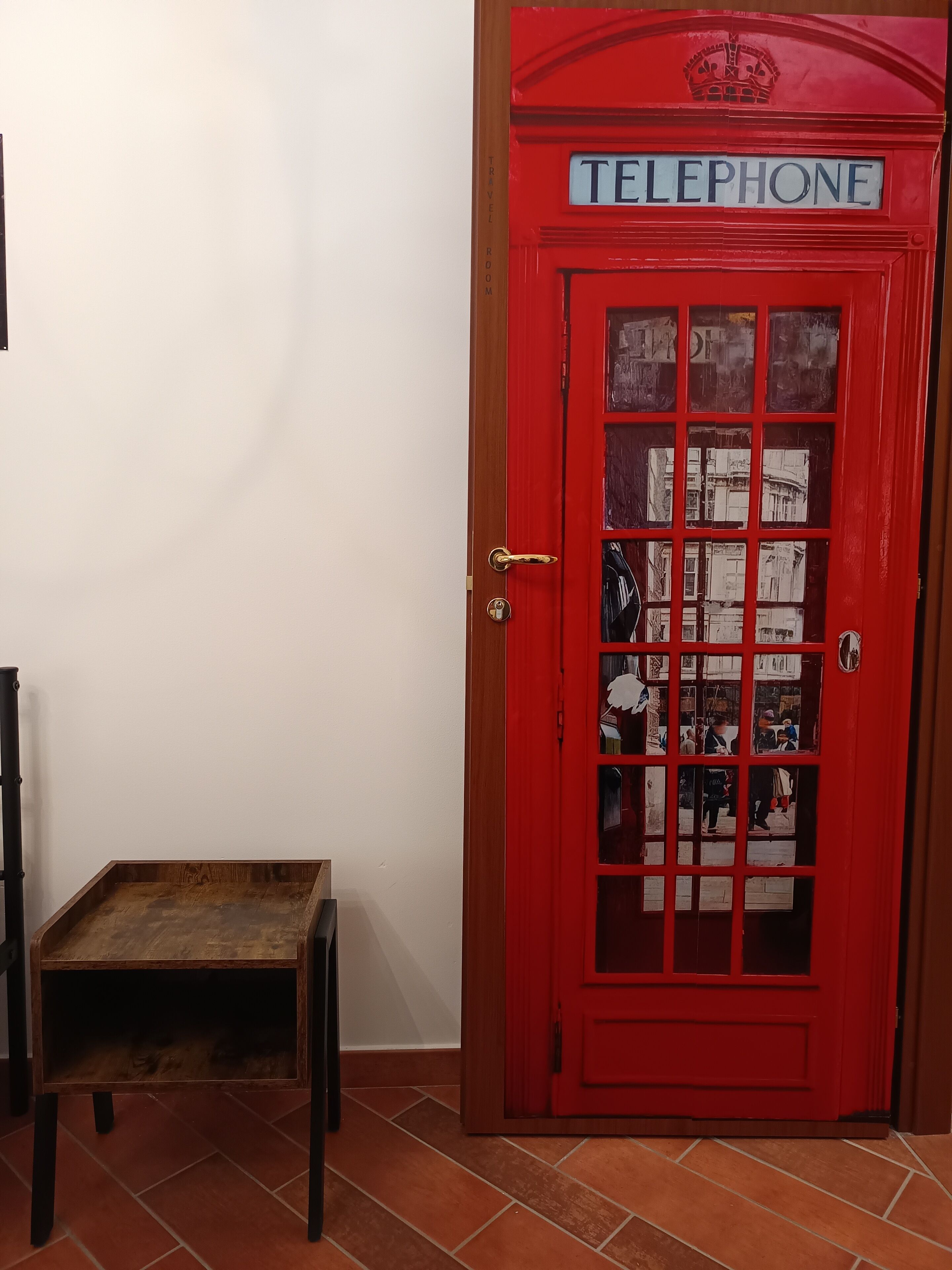 Une cabine téléphonique rouge avec une pancarte indiquant « TÉLÉPHONE » et une petite table en bois placée à côté.