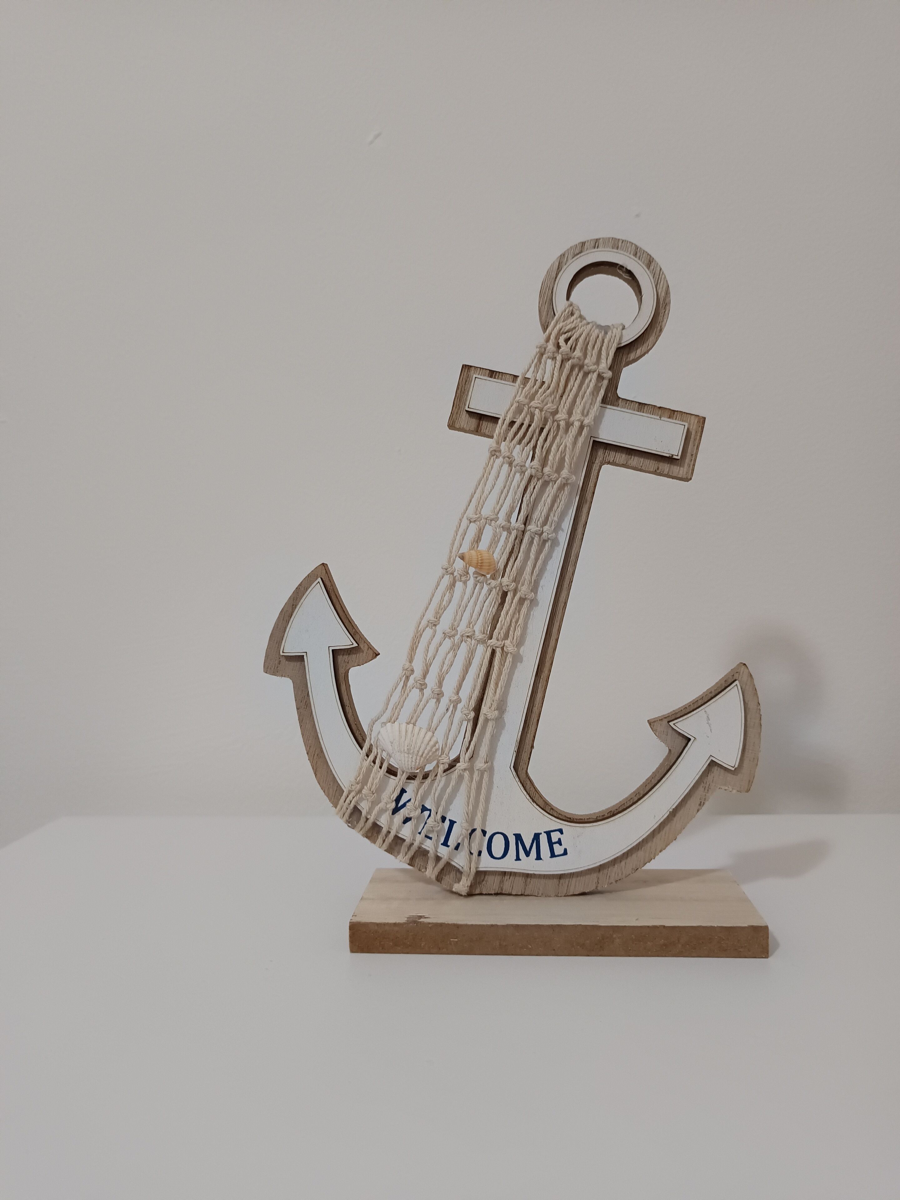 A wooden anchor with a macrame tassel and the word "WELCOME" on a flat base.