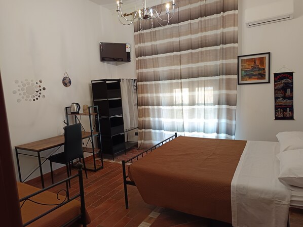 A bedroom with a bed, a desk, a chair, a wardrobe, a chandelier, and a curtain. - A casa di Peppe  (Palermo)