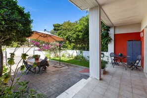 Eine Terrasse mit Tisch und Stühlen, umgeben von Kübelpflanzen und einem großen Sonnenschirm.