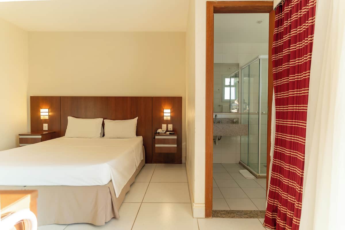 A hotel room with a large bed, bedside tables with lamps, a wooden headboard, and a bathroom visible through an open door.