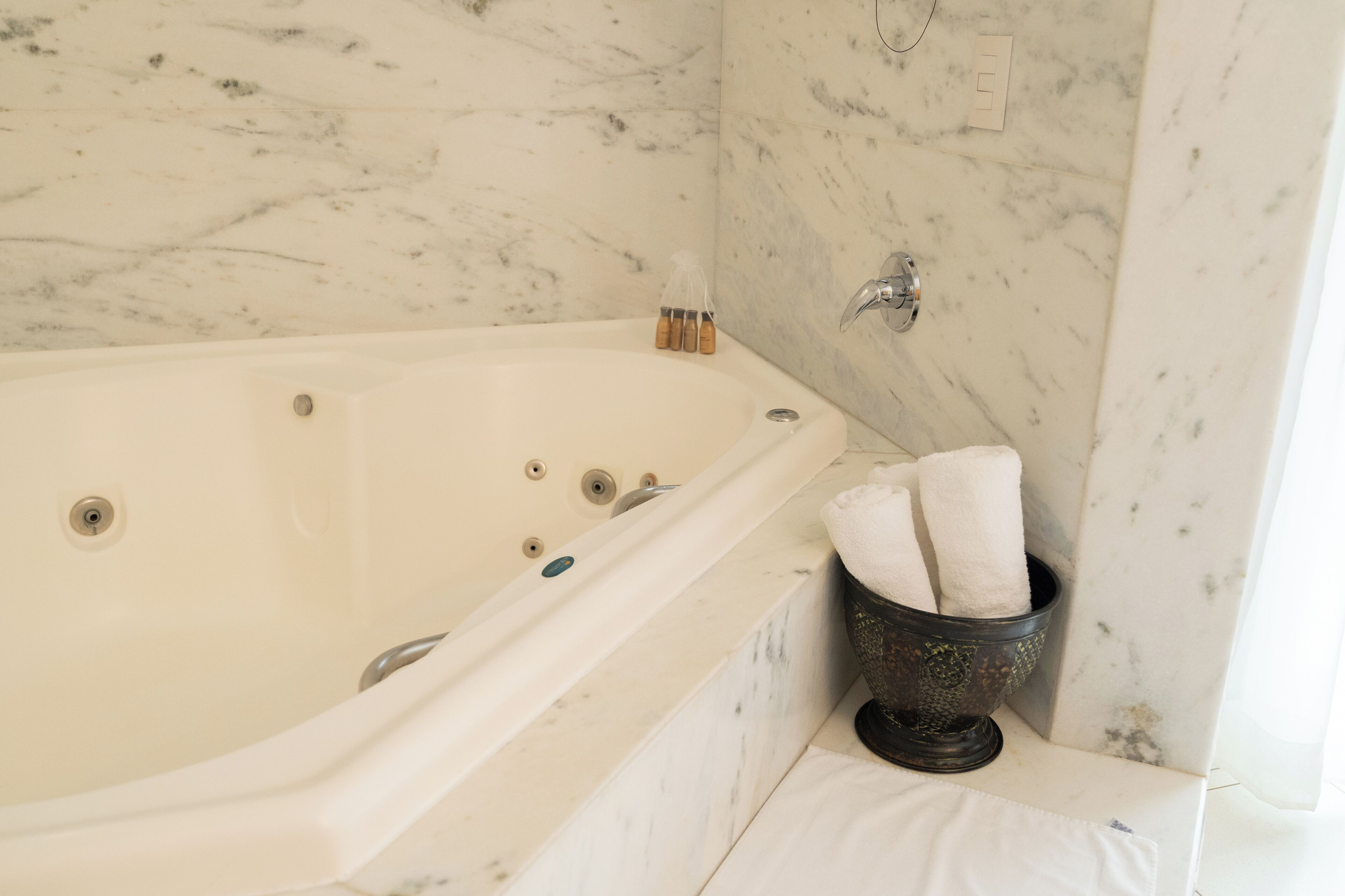 A bathroom with a marble wall, a bathtub, a towel rack, and a small decorative bowl.