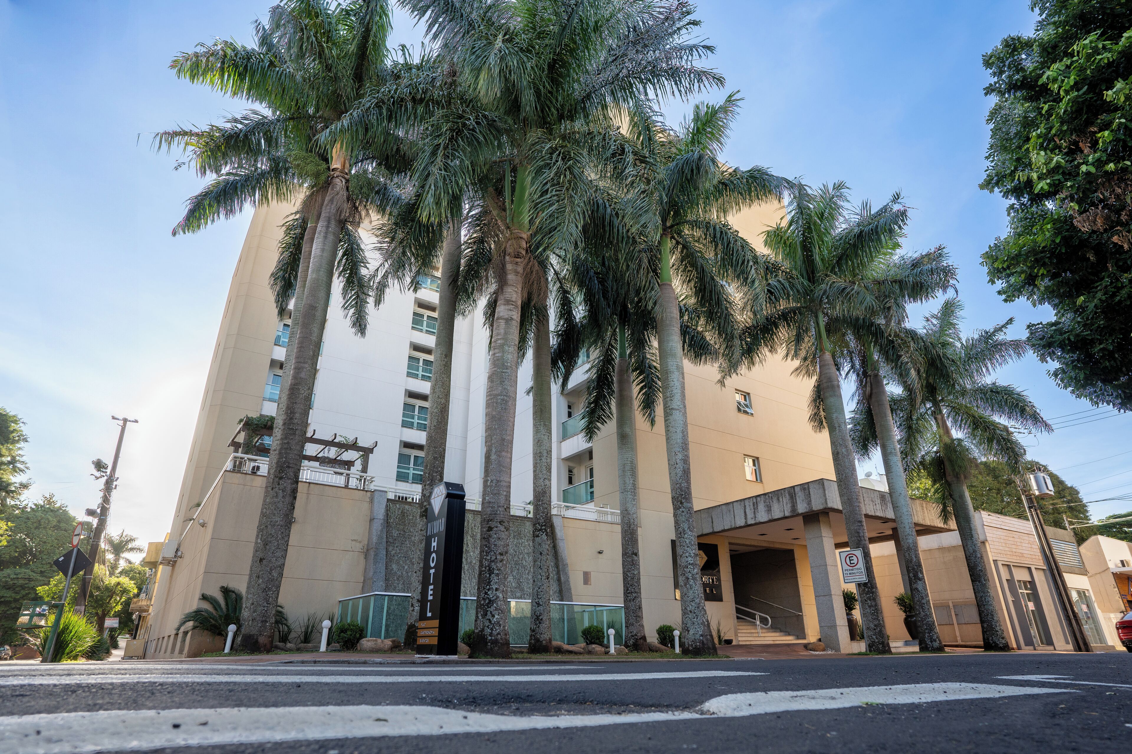 A hotel with a modern design, featuring tall palm trees in front, a prominent entrance, and a clear sky.
