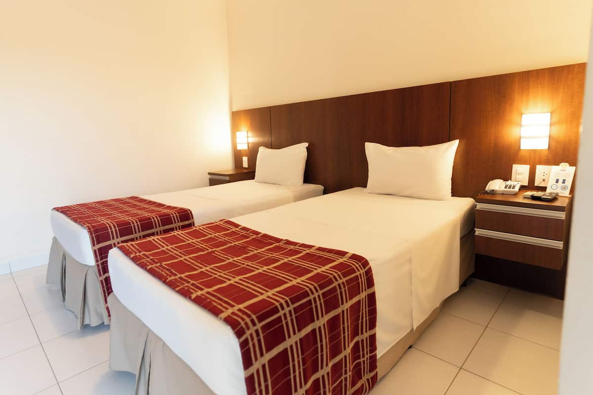 A hotel room with two beds, each with a white bedspread and a red checkered blanket. There are bedside tables with lamps and a phone.