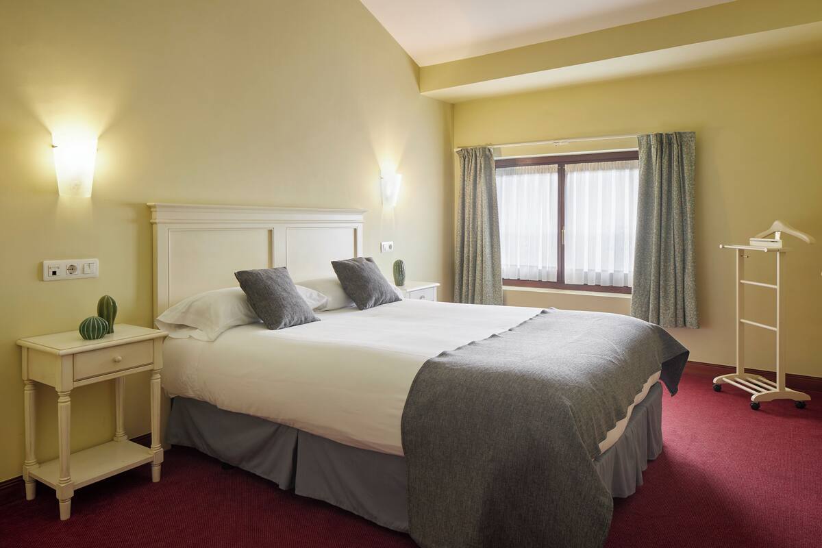 Ein Hotelzimmer mit Bett, Nachttischen, Vorhängen am Fenster und einem Kleiderständer.