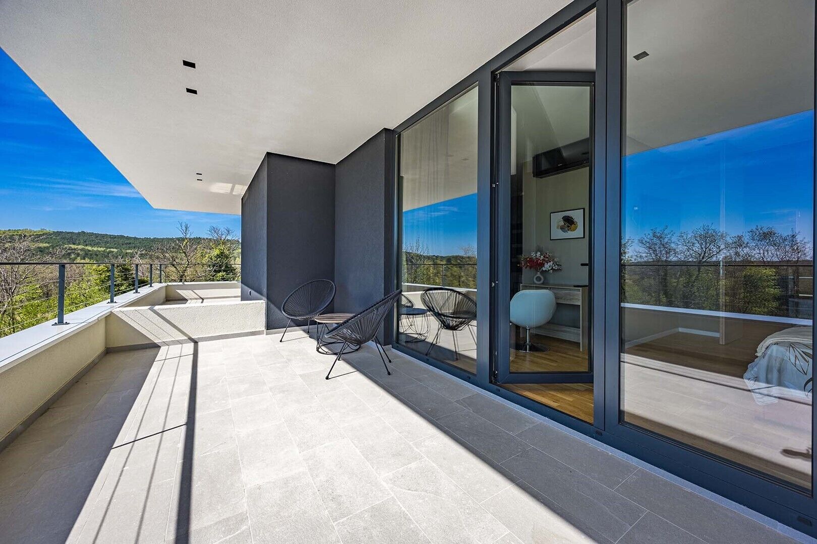 Ein moderner Balkon mit Glasdoor, zwei Stühlen und Blick auf die Landschaft.