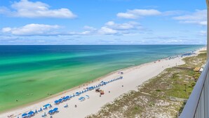 A beach with clear turquoise water, a sandy shore, and a row of blue umbrellas. - Ocean Reef 1005 Beachfront, Heated Indoor & Outdoor Pools, Hot Tub, FREE Golf (Panama City Beach)