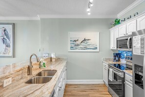 A modern kitchen with a marble countertop, stainless steel sink, and a microwave.