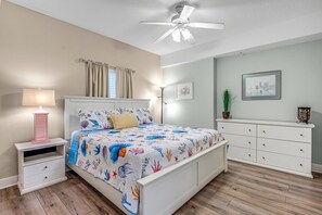 A bedroom with a bed, nightstands, a dresser, a ceiling fan, and a window with curtains.