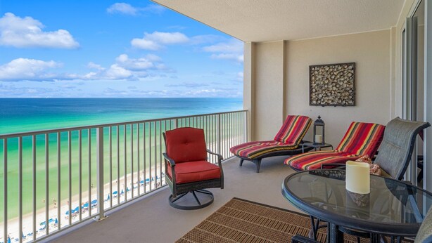 A balcony with a view of the beach, a glass table with a candle, and striped lounge chairs. - Ocean Reef 1005 Beachfront, Heated Indoor & Outdoor Pools, Hot Tub, FREE Golf (Panama City Beach)