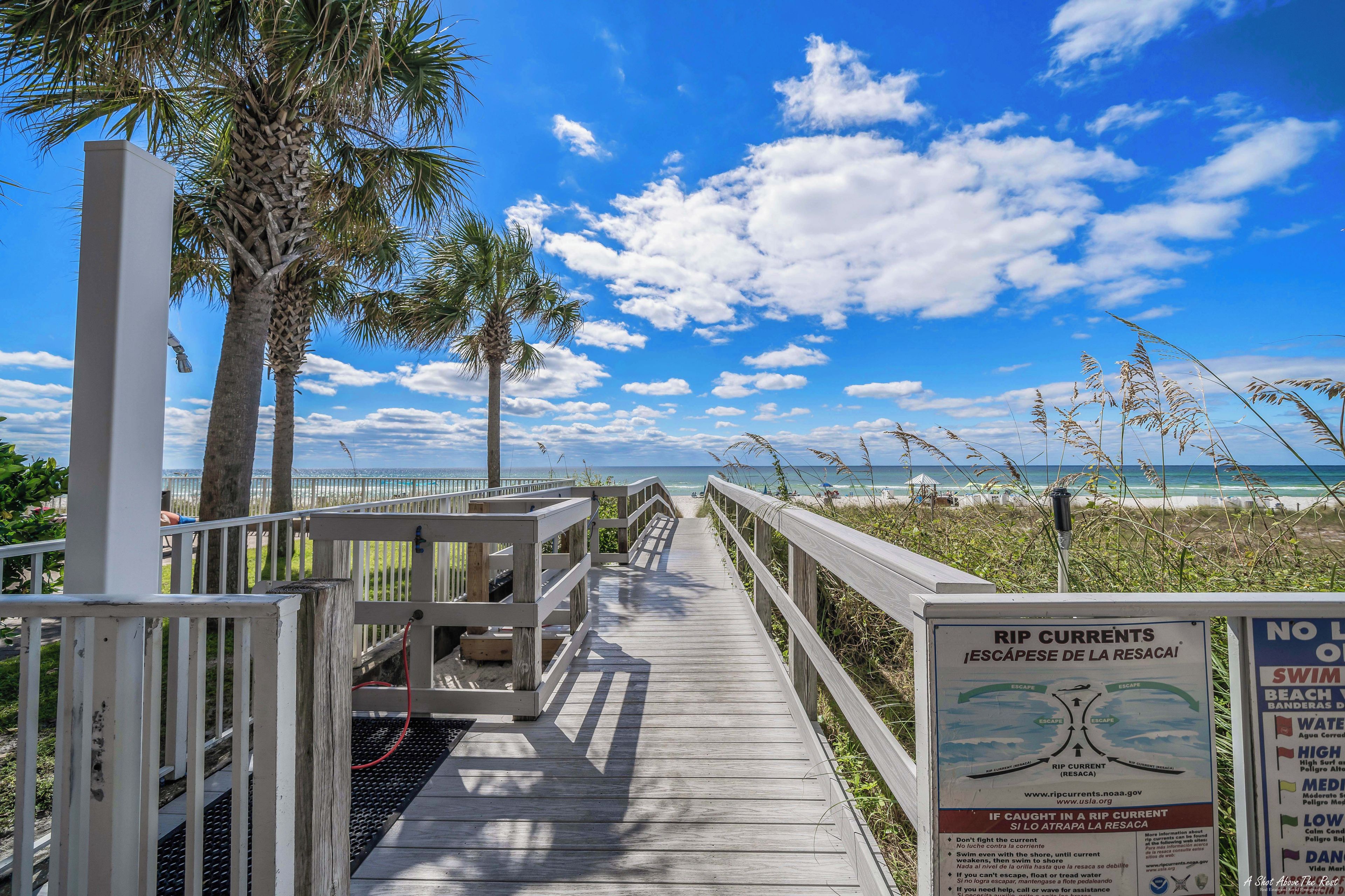 A wooden boardwalk leading to a beach with palm trees and a clear sky.