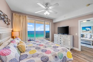 A bedroom with a bed, a TV, a ceiling fan, and a view of the ocean. - Ocean Reef 1005 Beachfront, Heated Indoor & Outdoor Pools, Hot Tub, FREE Golf (Panama City Beach)