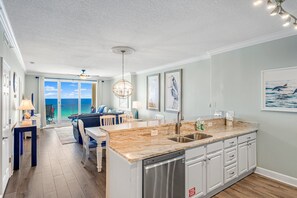 A modern kitchen with a large island, a dining area with a view, and a ceiling fan. - Ocean Reef 1005 Beachfront, Heated Indoor & Outdoor Pools, Hot Tub, FREE Golf (Panama City Beach)