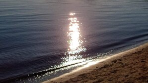 A calm body of water reflecting the sun with mountains in the background.