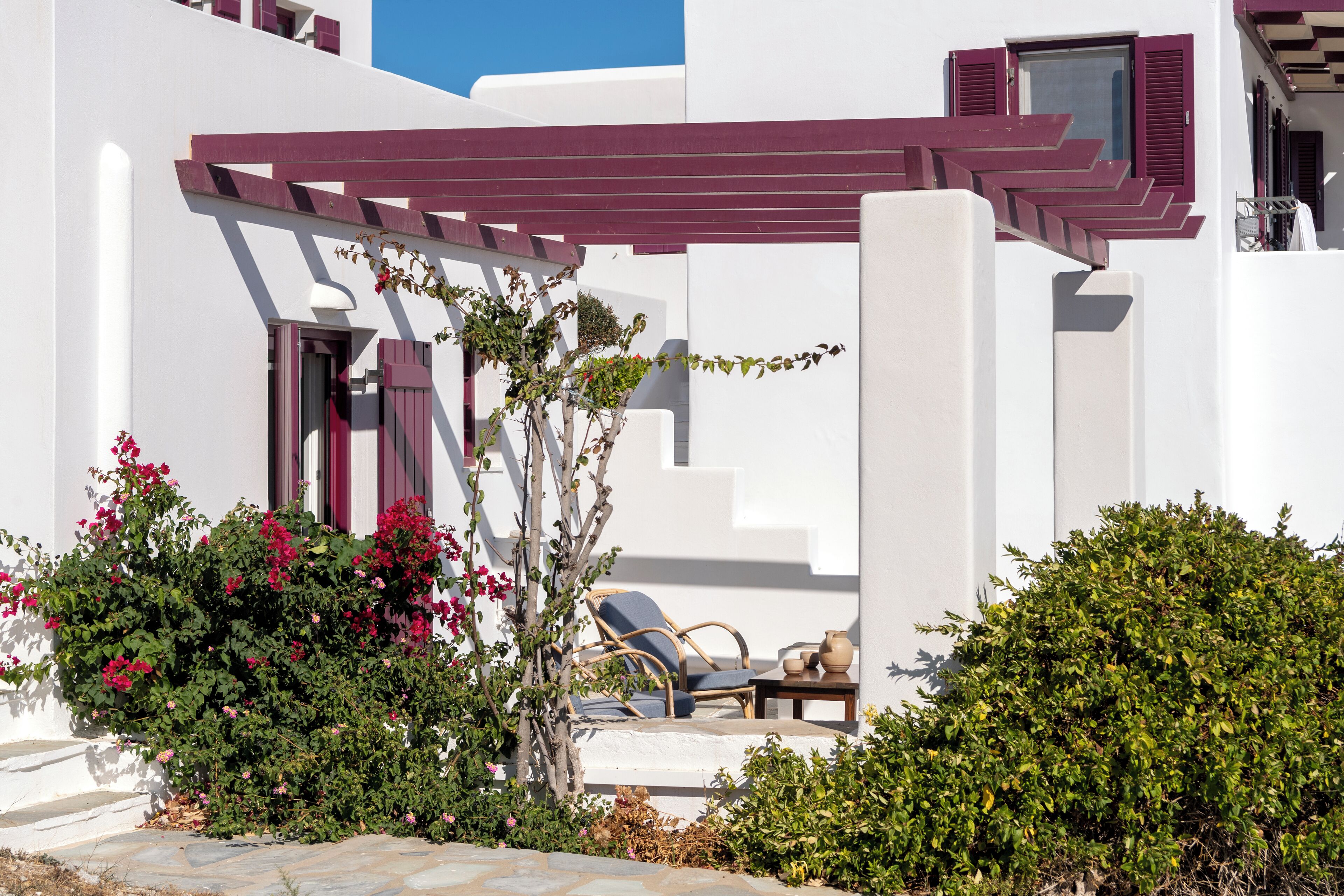 Ein weißes Gebäude mit einer roten Pergola, einem Stuhl und einem kleinen Tisch.
