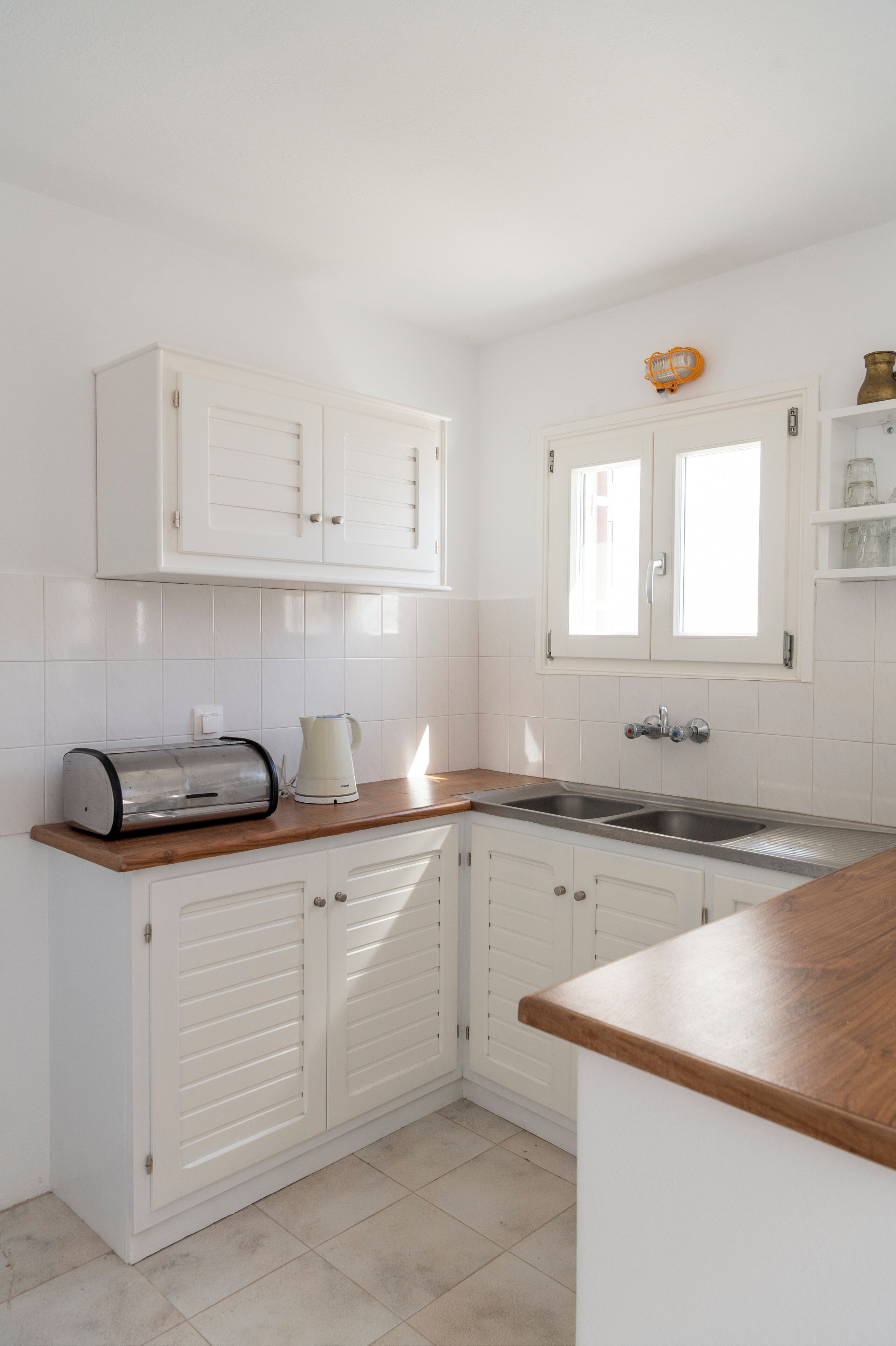 A kitchen with white cabinets, a wooden countertop, a toaster, a kettle, and a sink.