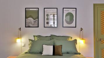 Ein Bett mit grüner Bettwäsche, ein Kopfkissen mit schwarzem Streifen und drei gerahmte Kunstwerke an der Wand.