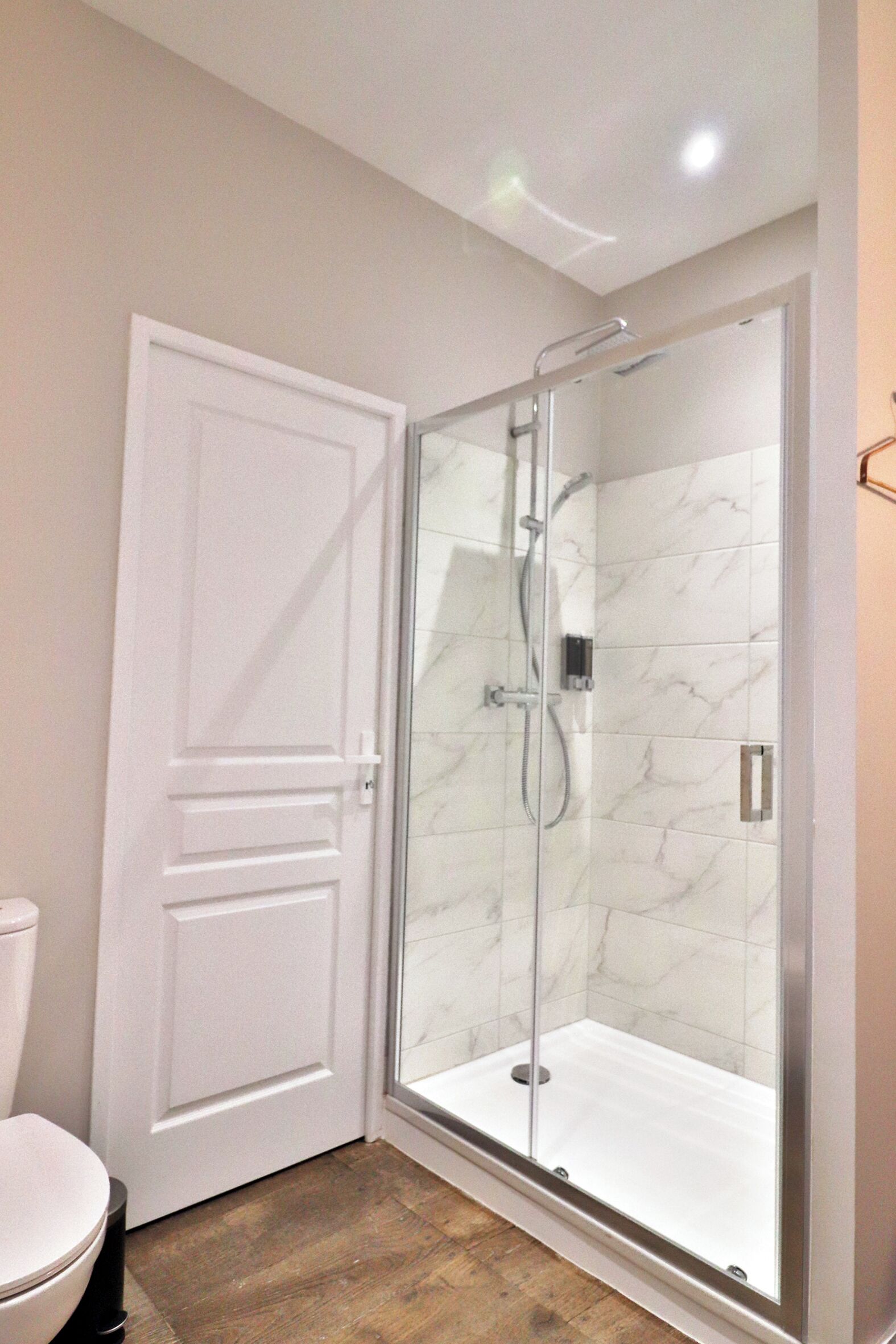 Une salle de bain avec une douche à parois de verre, des toilettes blanches et un plancher en bois.