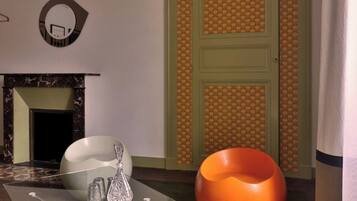 Una habitación moderna con una mesa de vidrio, una silla blanca, un sillón de peluche naranja y una puerta verde.