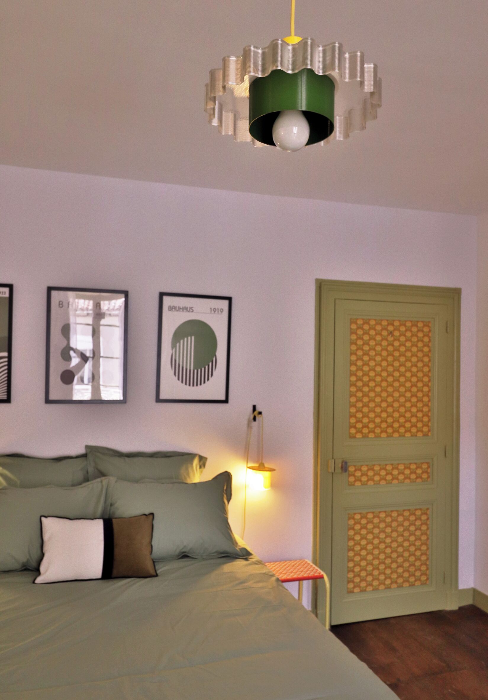 A bedroom with a bed, pillows, a bedside table, a lamp, and a door with a patterned panel.