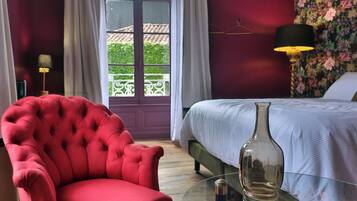 Habitación de hotel con un sillón rojo, una cama con ropa de cama blanca y una mesita de centro de cristal, con vistas a zonas verdes.