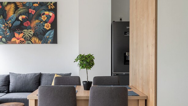Una sala moderna con comedor, una gran obra de arte tropical y una planta en maceta.