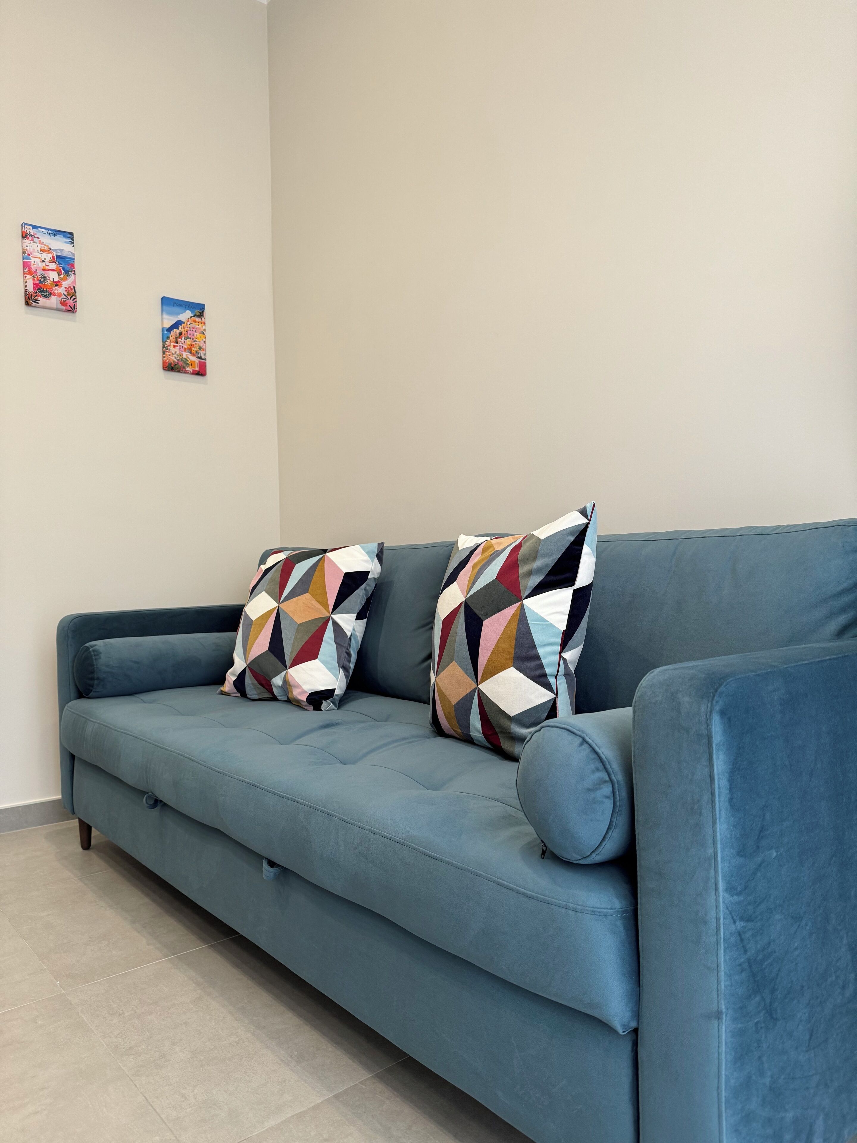 En blå soffa med mönstrade kuddar och två små tavlor på väggen.