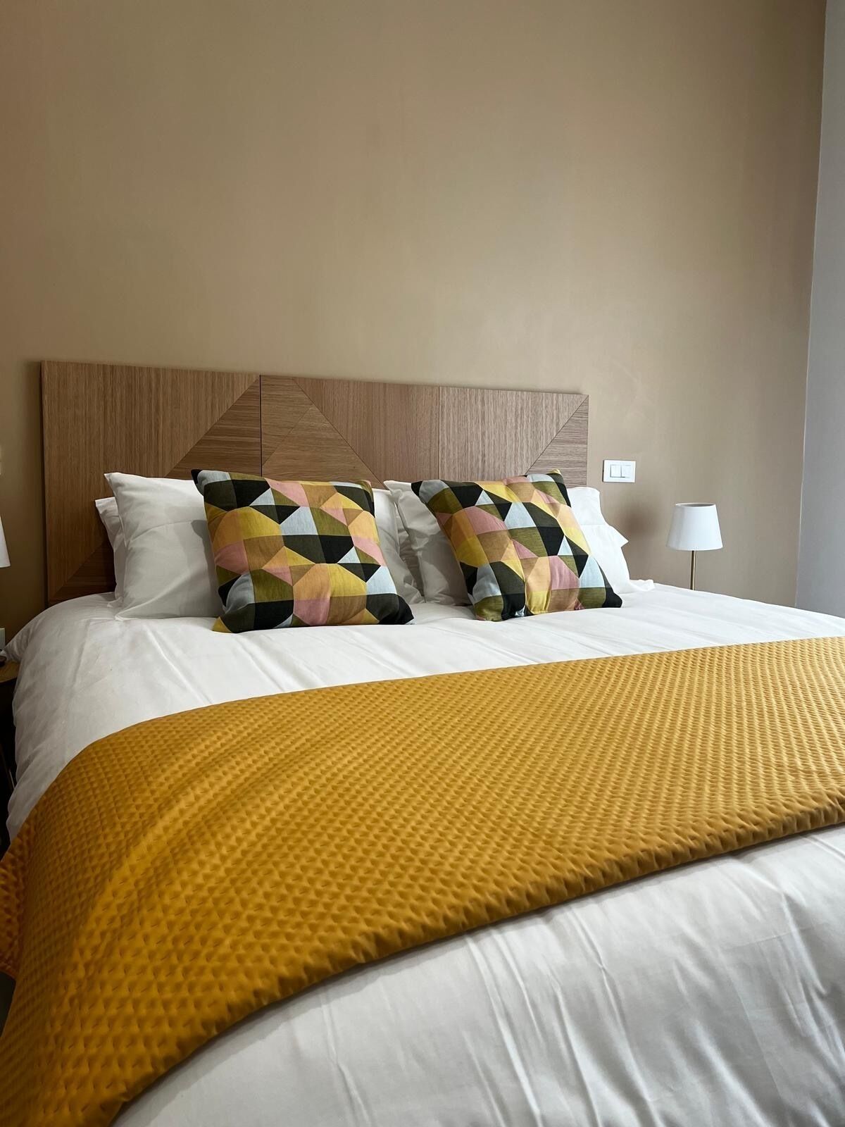 A neatly made bed with a geometric patterned pillow, a plain white pillow, and a yellow textured blanket.