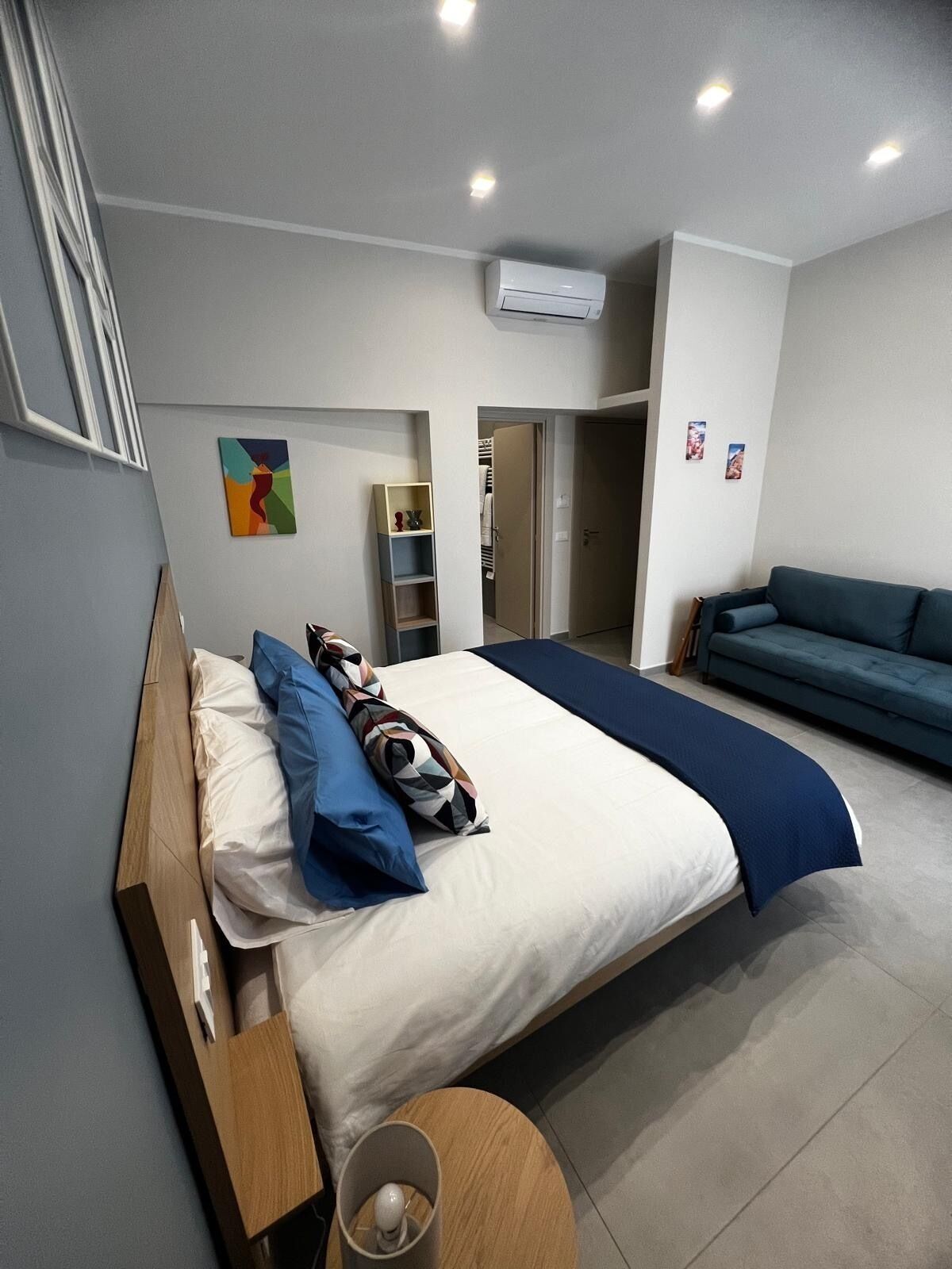 Een moderne slaapkamer met een groot bed, een blauwe bank, een tafeltje en een kledingkast.