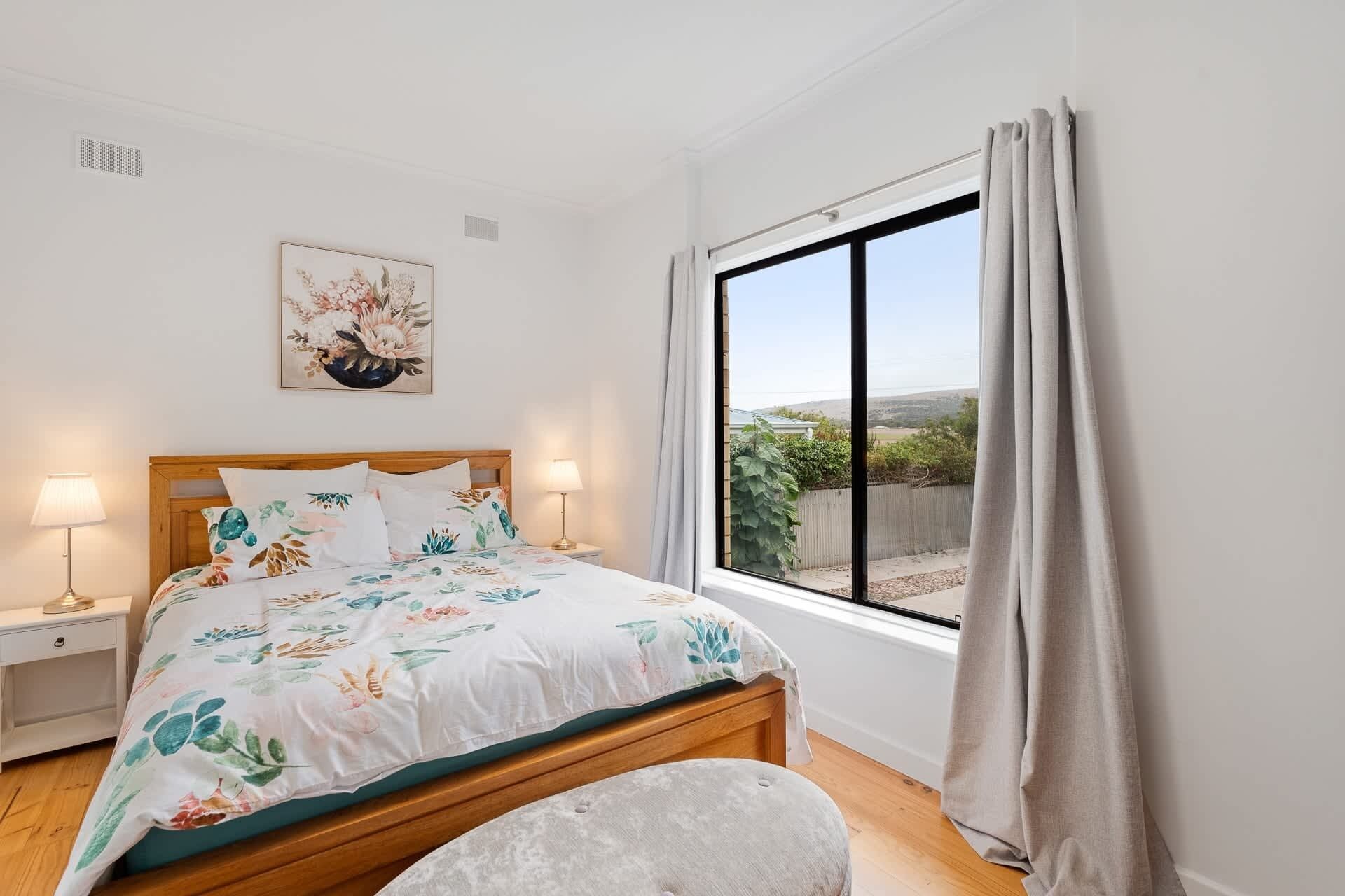Een slaapkamer met een bed, twee nachtkastjes, een raam met gordijnen en een schilderij aan de muur.