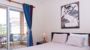 Une chambre à coucher avec un lit, une table de chevet avec une lampe, un tableau au mur et un balcon avec une chaise et une table.
