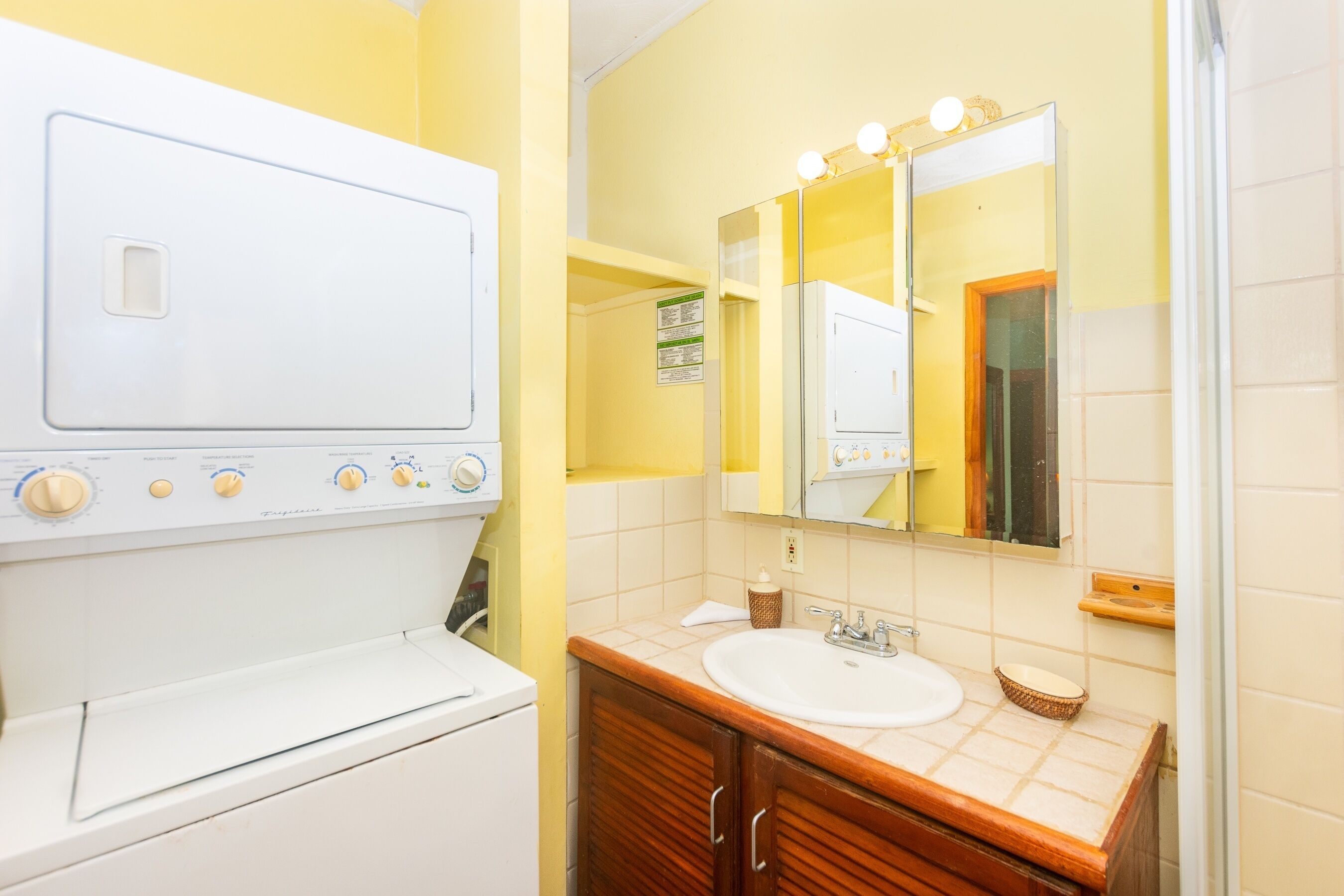 A compact bathroom with a white washing machine, a sink with a mirror, and wooden cabinets.