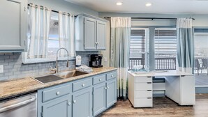 A modern kitchen with light blue cabinets, a granite countertop, a built-in dishwasher, and a coffee maker. - Shore Better Than Work 4 Bedroom Home by RedAwning (Rockport)