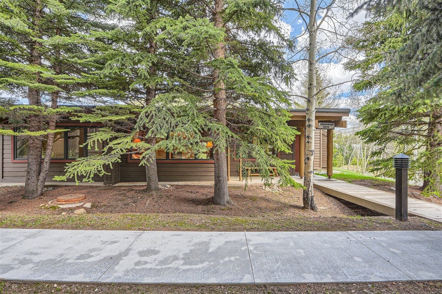 A modern cabin with a wooden deck, surrounded by evergreen trees.