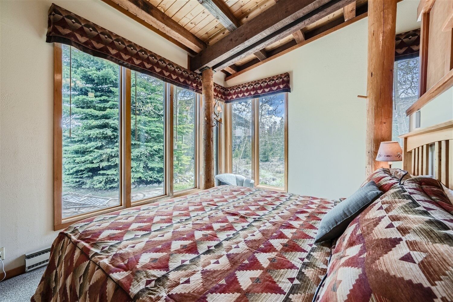 A bedroom with a large bed, multiple windows, and a view of trees.
