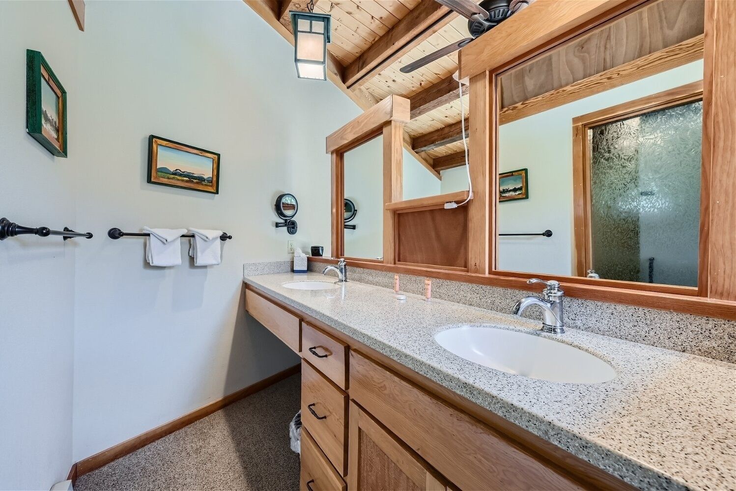 A bathroom with two sinks, wooden cabinets, a large mirror, and framed pictures on the wall.